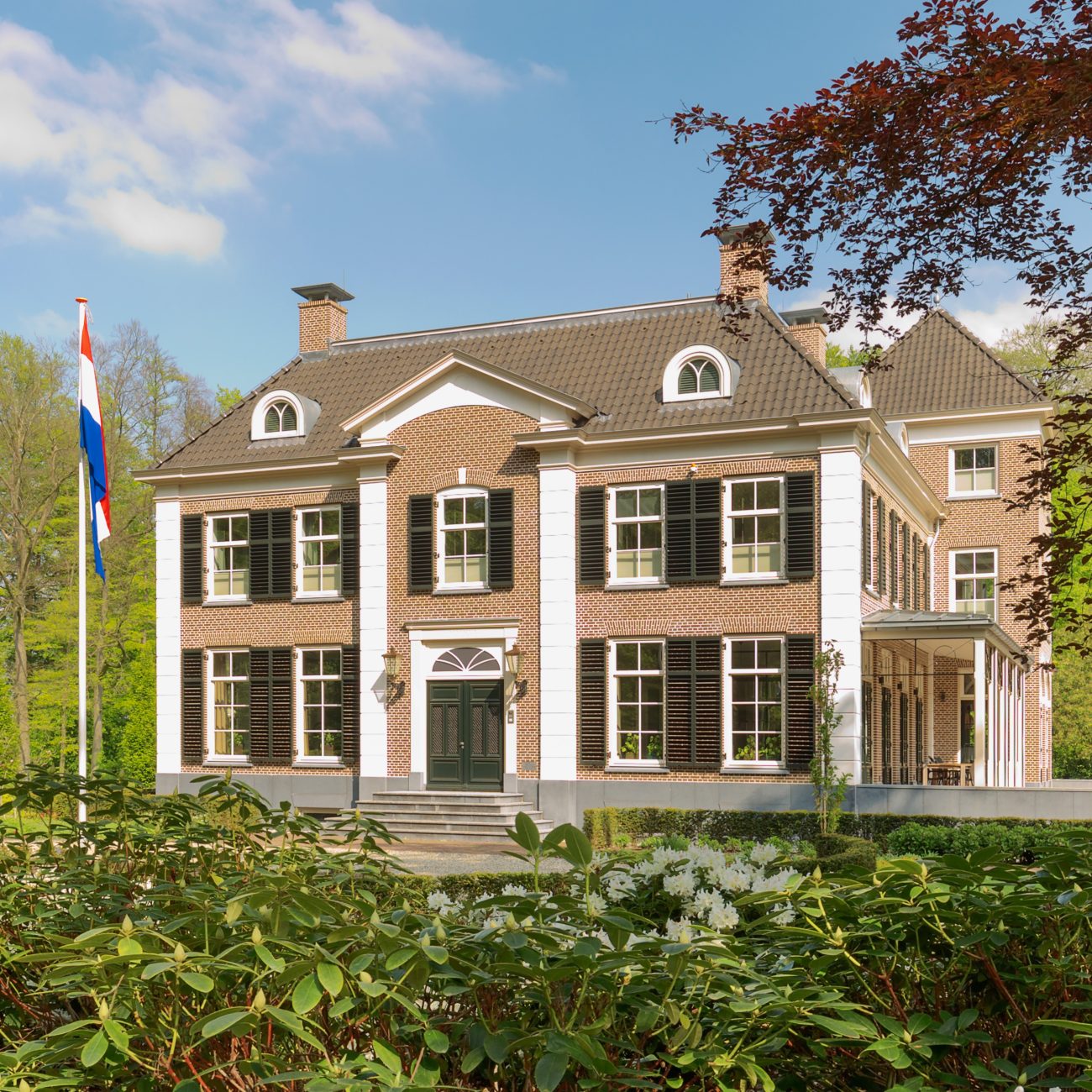Neoclassicistisch landhuis Bruggenbosch in Twello met symmetrische voorgevel, luiken en klassieke details in groene parkachtige omgeving